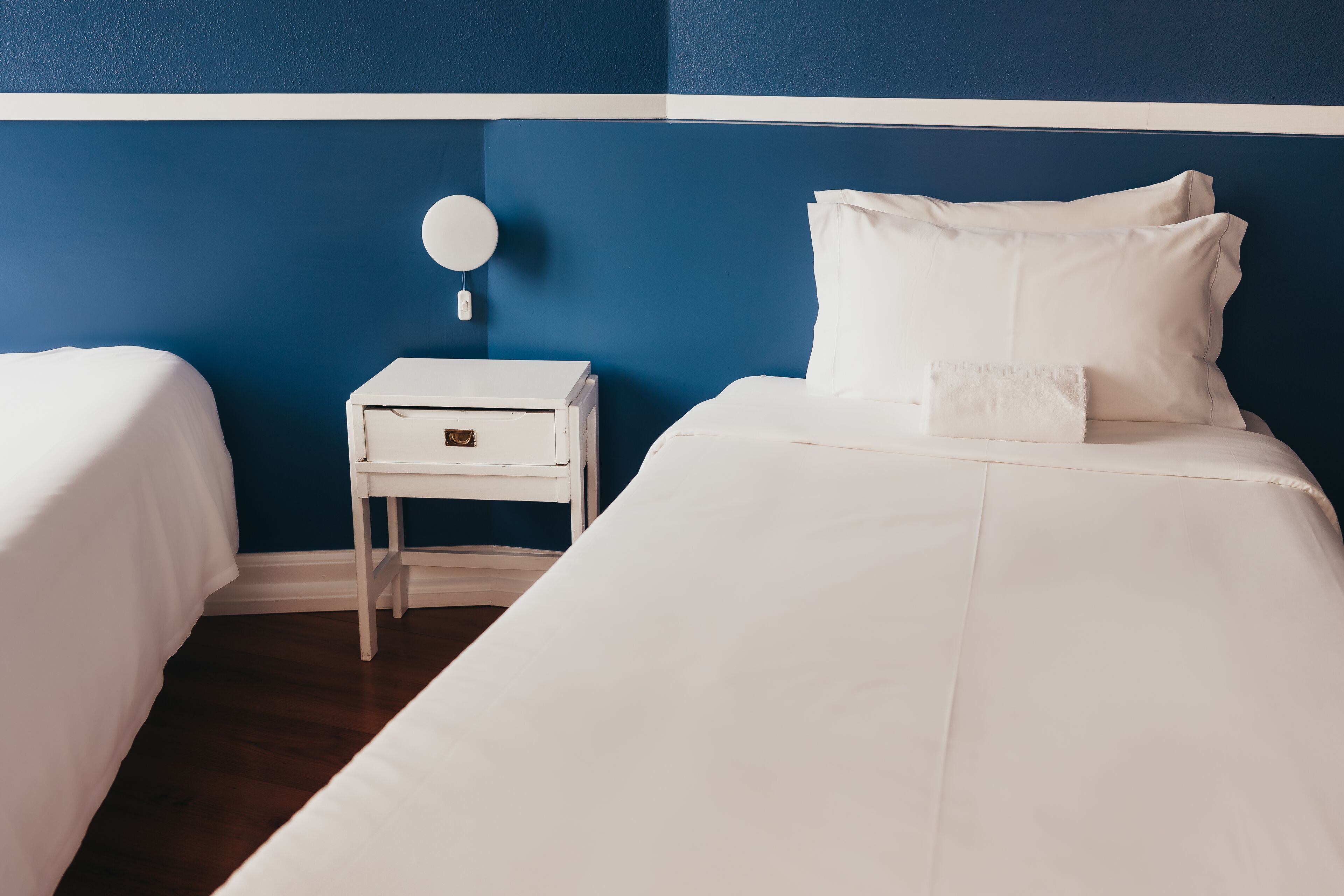 Una habitación de hotel con dos camas, una mesita de noche blanca y un espejo redondo.