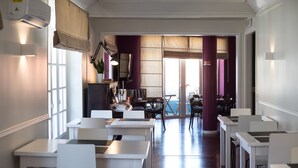A hotel lobby with white tables and chairs, a reception desk, and a view of the outdoor seating area. - Hotel Leiria Classic (Leiria)