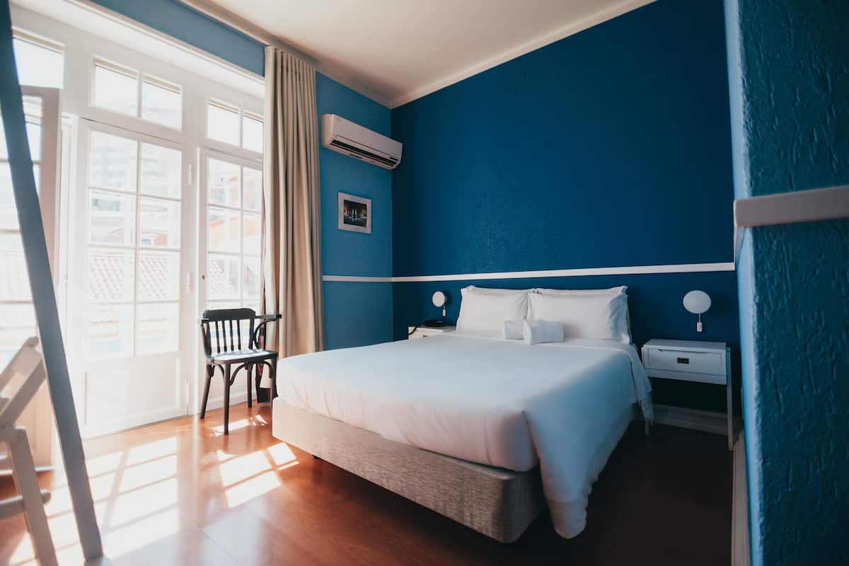 Ein Schlafzimmer mit einem Bett, Nachttischen, einem Sessel und einem Fenster mit Vorhängen.