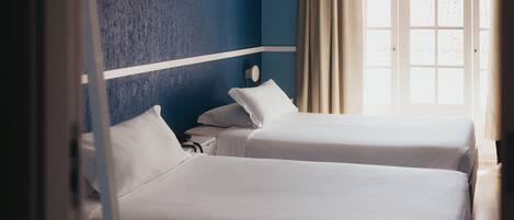 Habitación de hotel con dos camas, una pared azul decorativa y una ventana con cortinas.