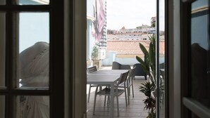 An open door to a balcony with a table and chairs, potted plants, and a view of buildings in the background. - Hotel Leiria Classic (Leiria)