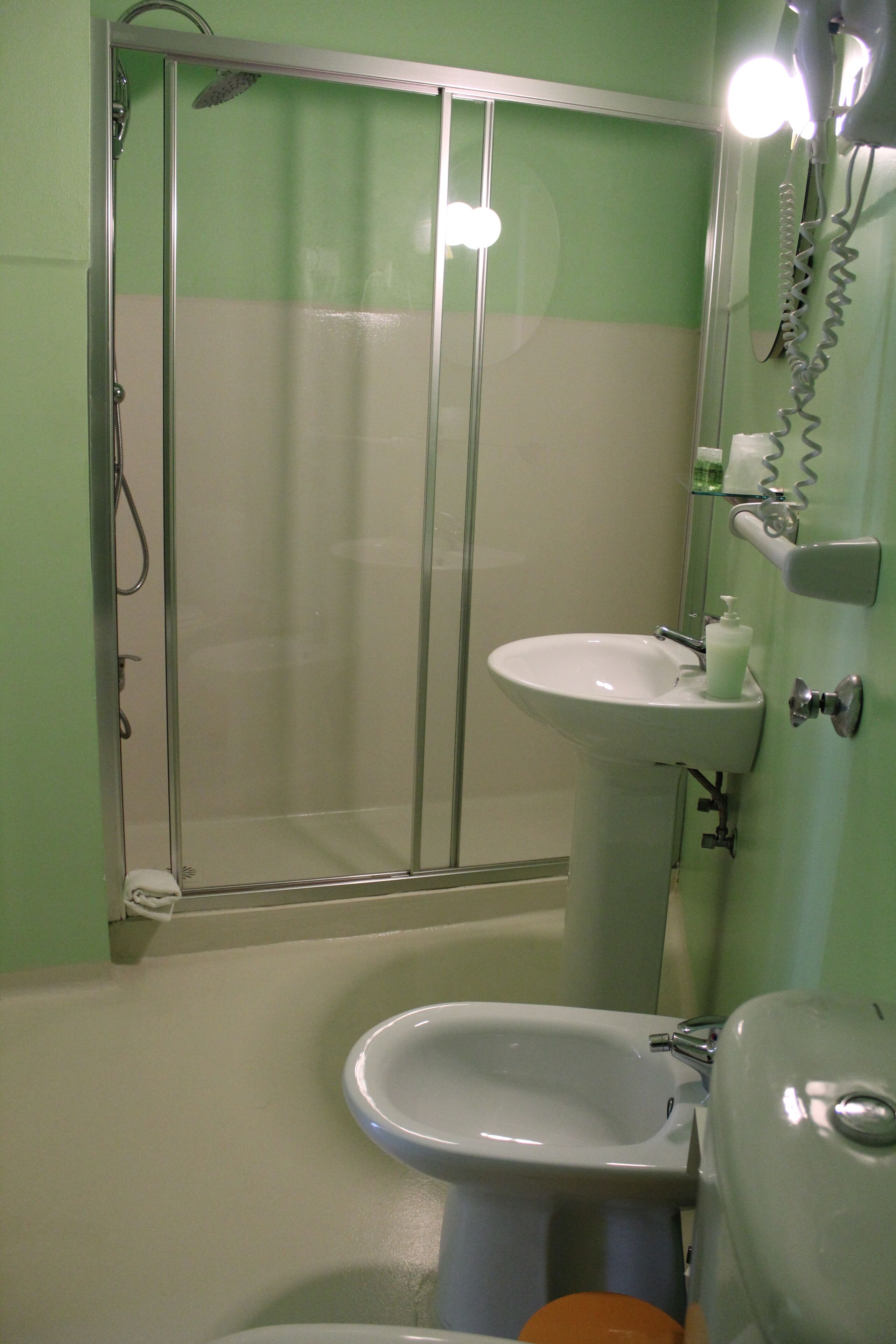 Un bagno con doccia vetro, lavabo su piedistallo e water.