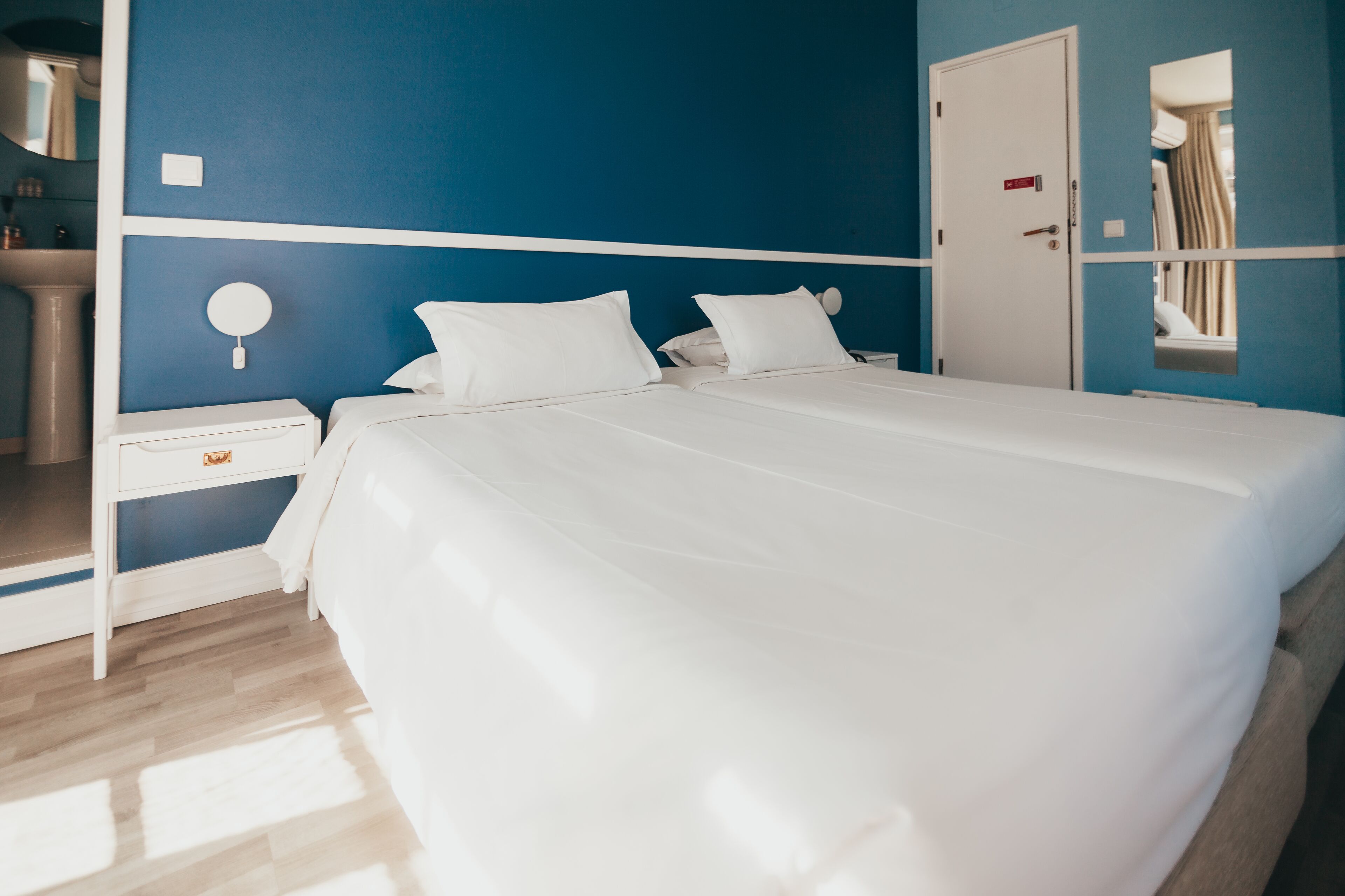 Una habitación de hotel con una cama grande, una mesita de noche, un espejo y una puerta.