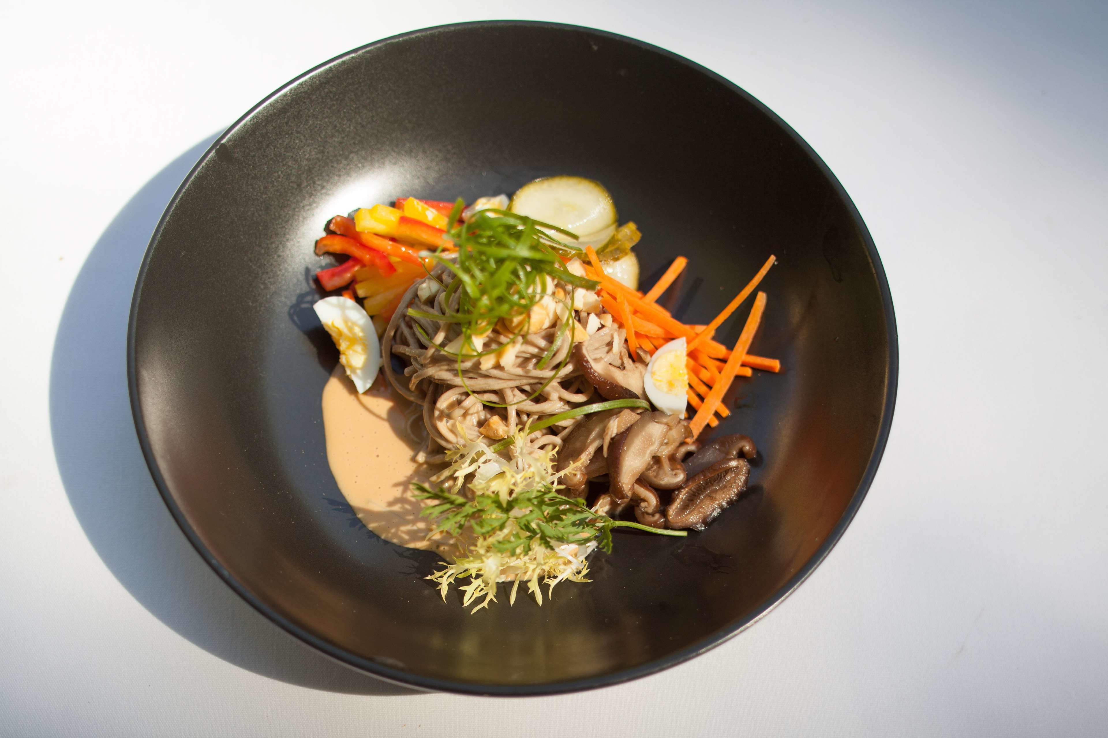 A bowl of noodles with vegetables and a boiled egg.