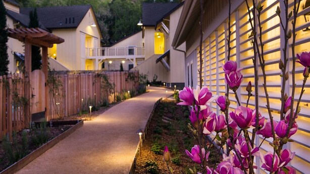 A pathway leading to a building with a wooden fence and flowering plants. - Farmhouse Inn (Forestville)