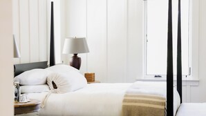 A neatly made bed with pillows, a bedside lamp, a bedside table with a glass, and a window with curtains. - Farmhouse Inn (Forestville)
