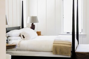 A neatly made bed with pillows, a bedside lamp, a bedside table with a glass, and a window with curtains. - Farmhouse Inn (Forestville)