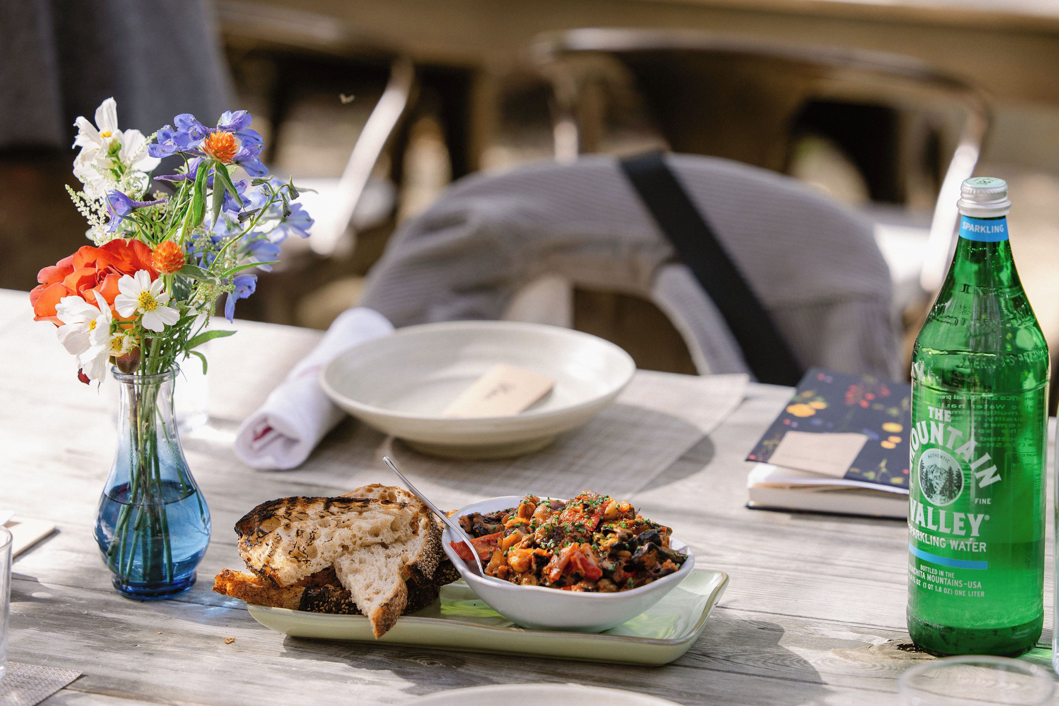 A table with a bowl of food, a bottle of sparkling water, and a vase of flowers.