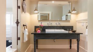 Un baño con tocador de madera oscura, un espejo grande, dos lámparas colgantes y un lavabo blanco.