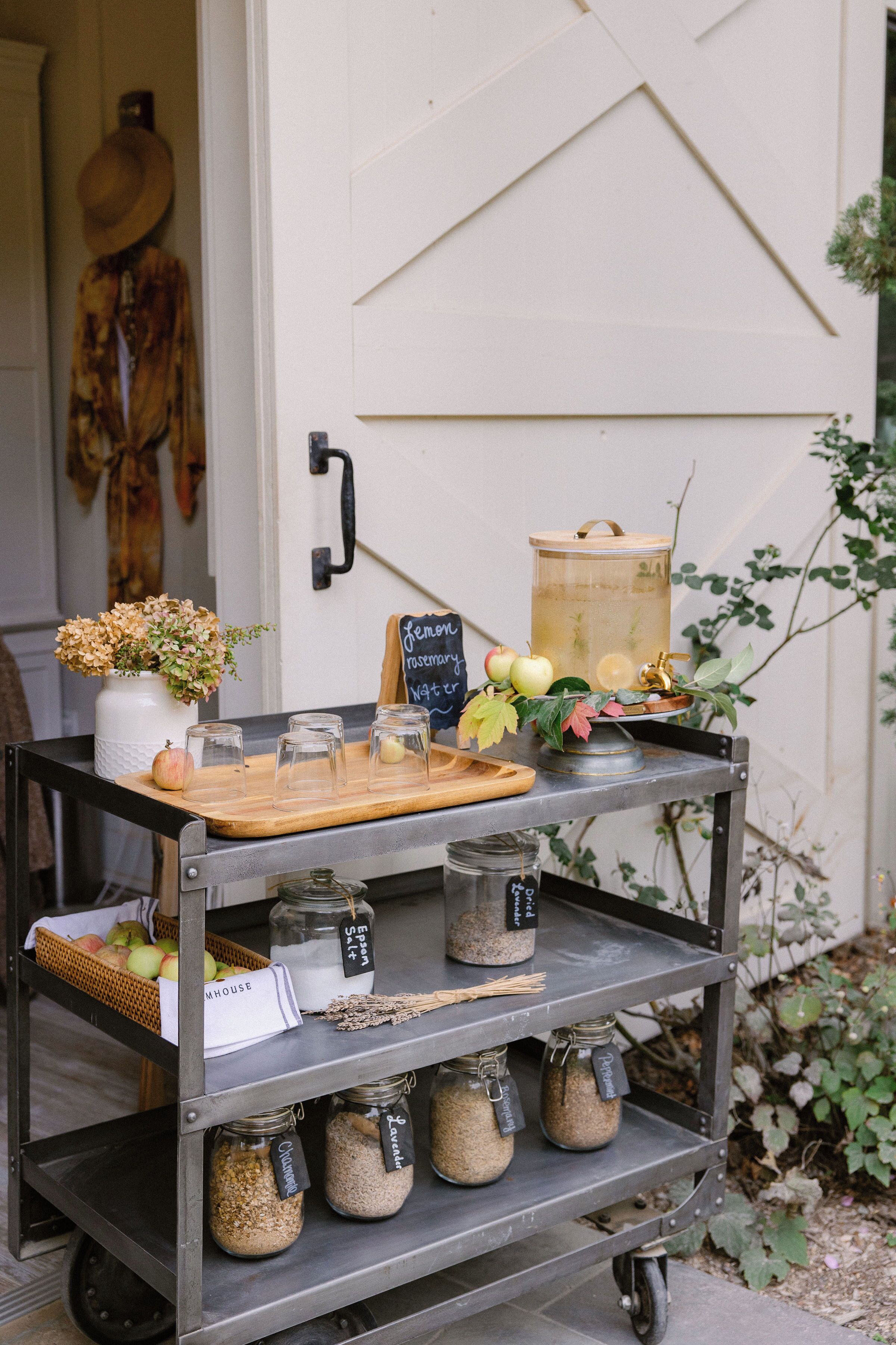 A metal cart with jars labeled 'Chardonnay,' 'Chardonnay,' 'Chardonnay,' and 'Chardonnay,' a wooden tray with apples and a vase of flowers, and a chalkboard sign with 'feminine' and 'rosé' written on it.