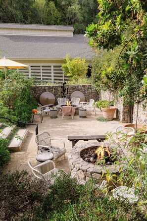 An outdoor patio with stone walls, a fire pit, and white wicker furniture.