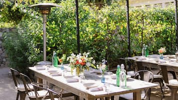An outdoor dining area with tables and chairs, surrounded by greenery and a pergola structure.