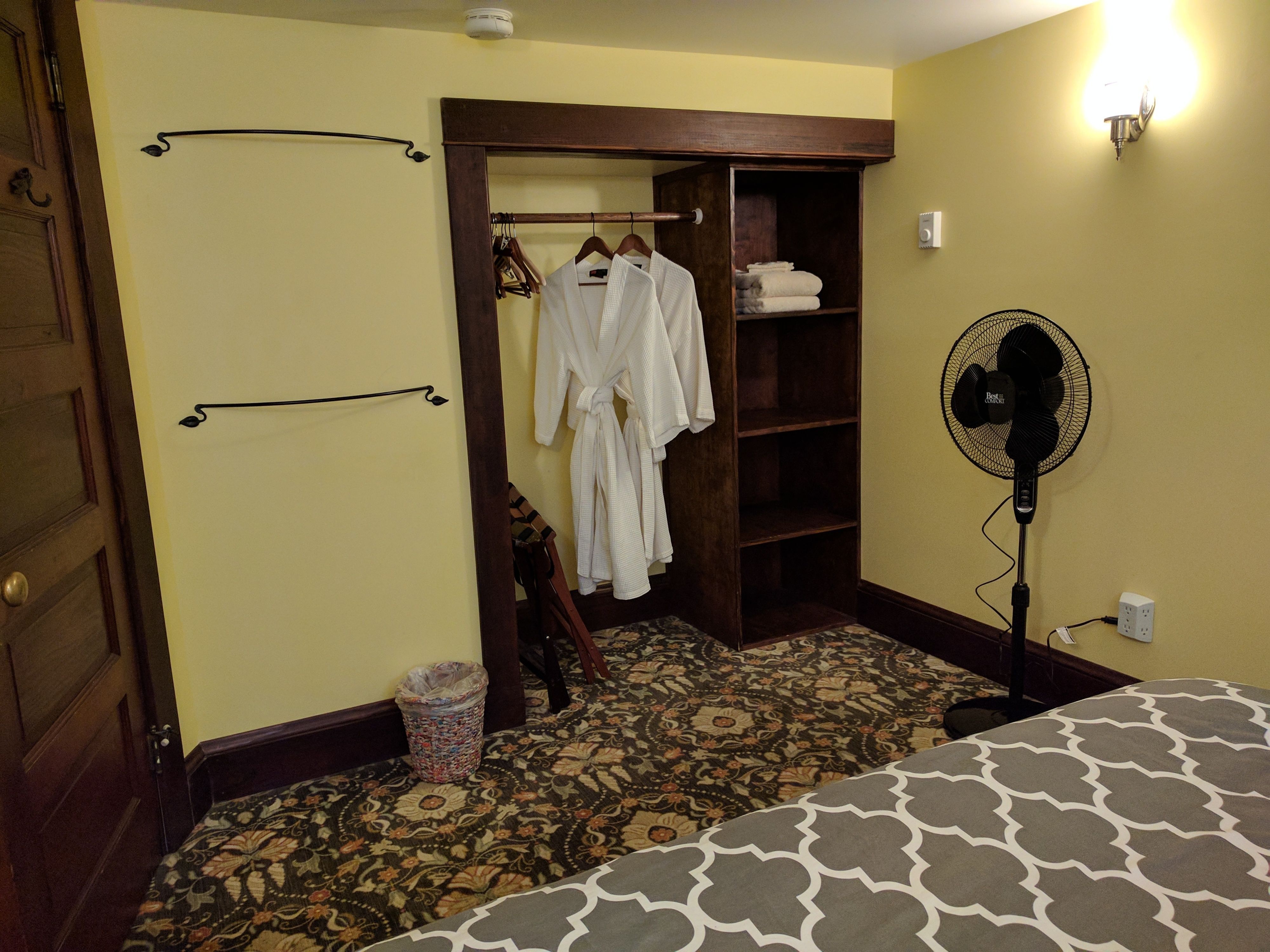 Hotelkamer met een bed, een garderobe, een spiegel, een ventilator en een kamerbreed tapijt met dessin.