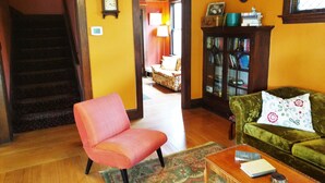A living room with a staircase, a green sofa, a wooden coffee table, and a bookshelf. - Bluebird Guesthouse (Portland)