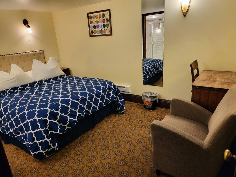 Quarto de hotel com cama, cadeira, lixeira, espelho e quadro na parede.