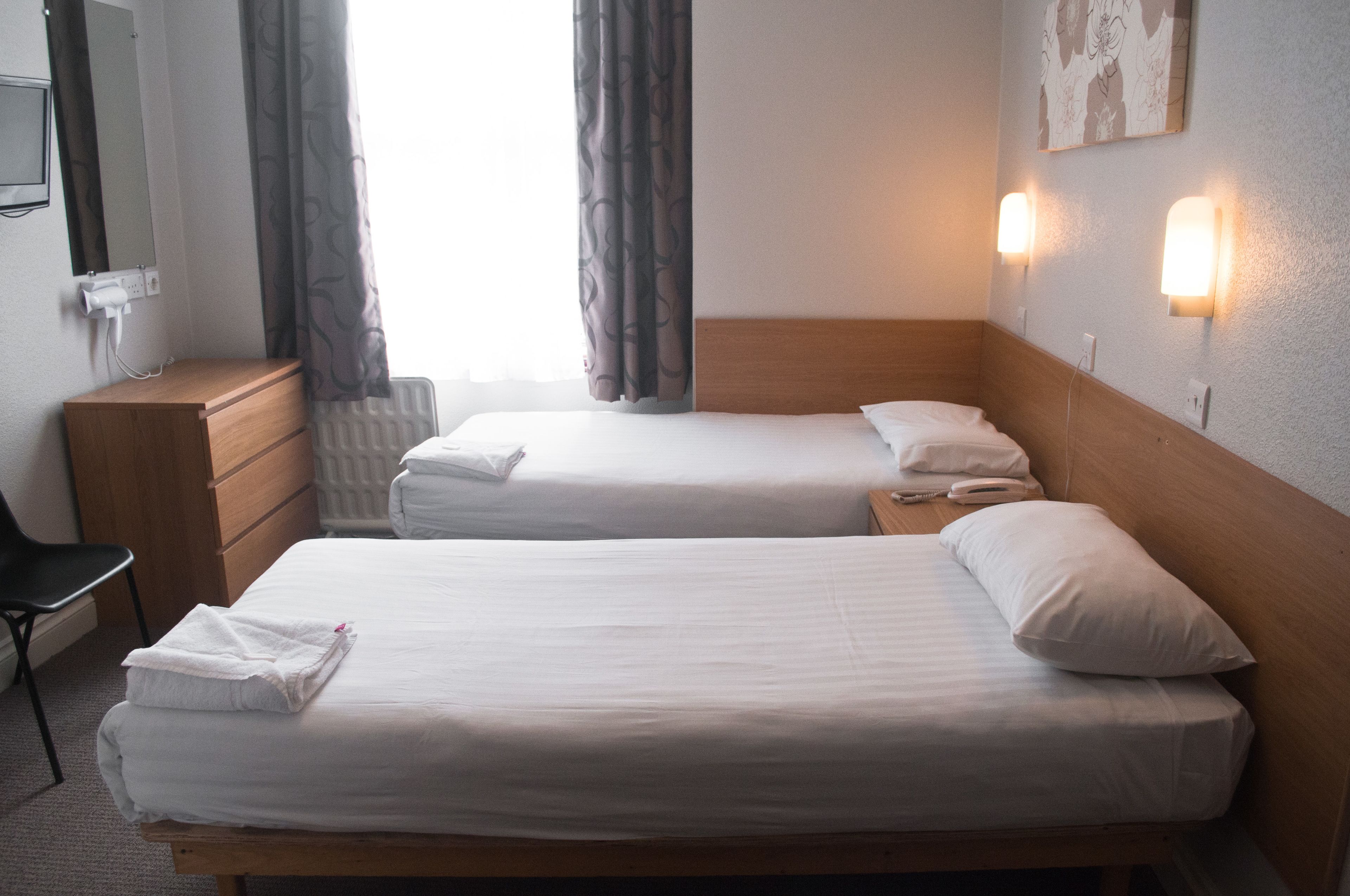 A hotel room with two single beds, a wooden dresser, a chair, and a radiator.