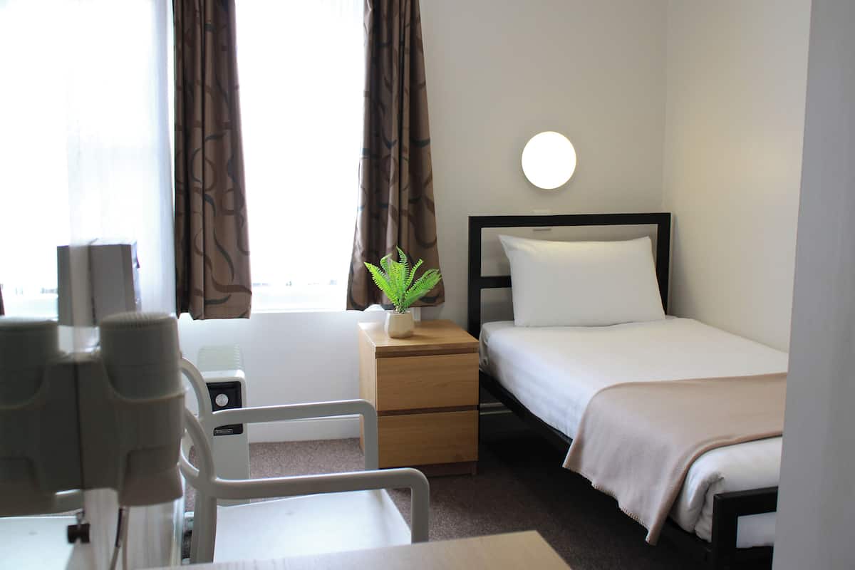 Una habitación de hotel con cama, mesita de noche, lámpara y una planta en maceta.