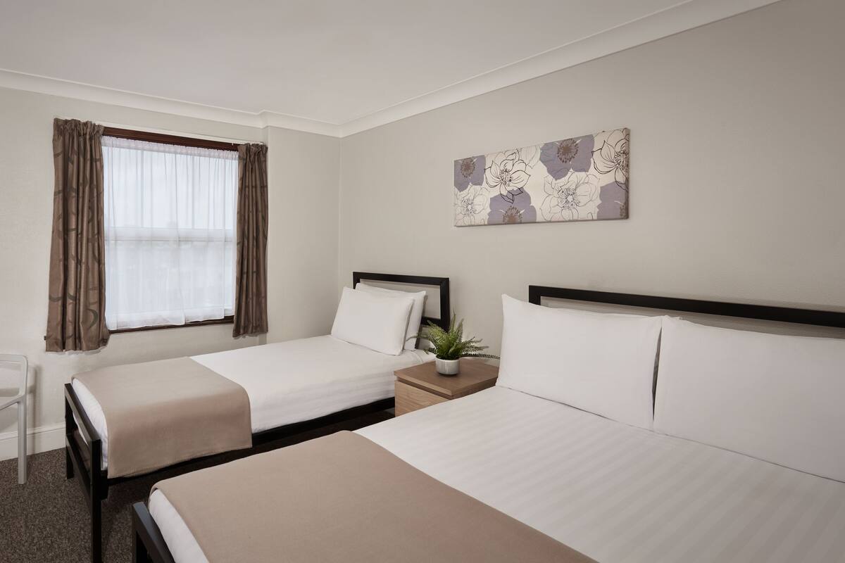 Habitación de hotel con dos camas, un escritorio, una silla y un ventanal con cortinas.