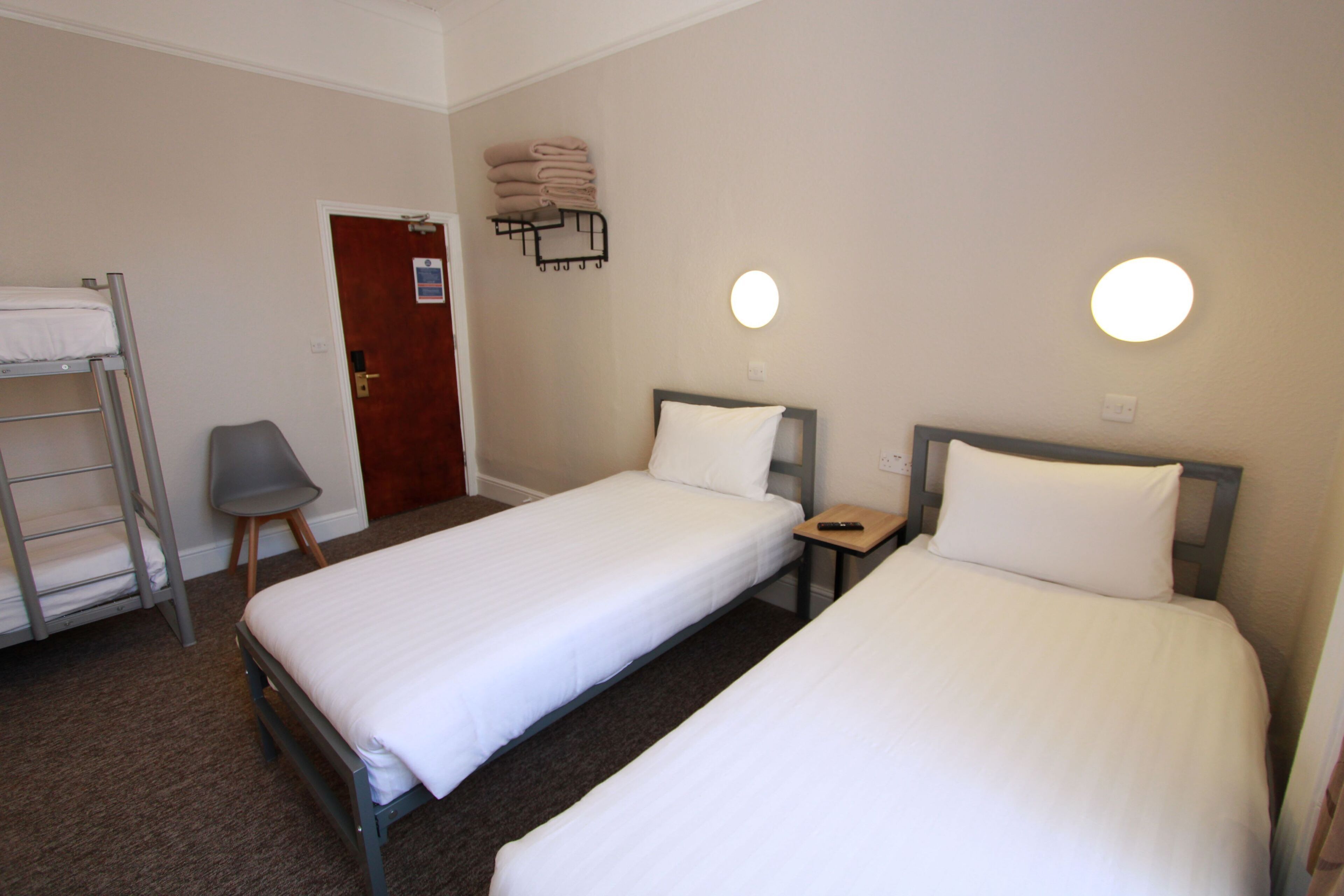A hotel room with two single beds, a small desk, a chair, a ladder, and a wall-mounted towel rack.