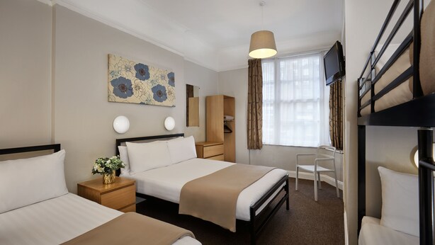 Habitación de hotel con dos camas, un escritorio, una silla, un televisor y una ventana con cortinas.