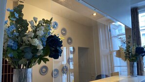 Zona de recepción con mostrador, un espejo grande que refleja el interior, y un florero con flores sobre el mostrador.