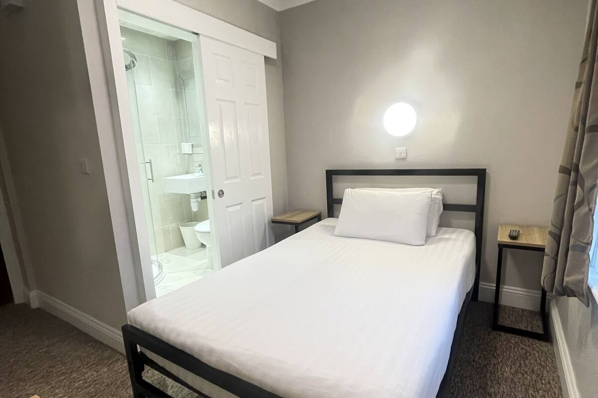 Un dormitorio con cama, mesita de noche, armario y baño con puerta de cristal.