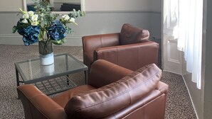 Una habitación con un sofá de cuero marrón, una mesa de centro de vidrio y un jarrón con flores.