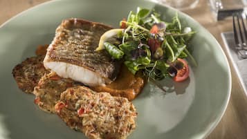 A plate with a piece of grilled fish, a slice of bread, and a side salad.
