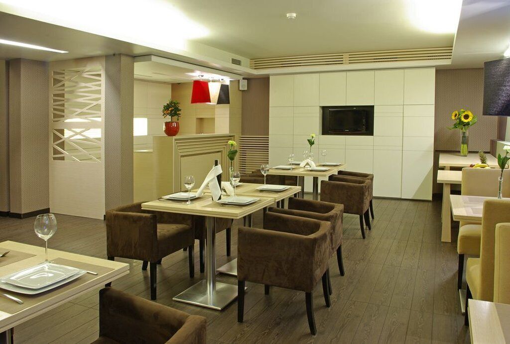 A modern dining area with multiple tables and chairs, a TV mounted on the wall, and decorative elements like plants and flowers.
