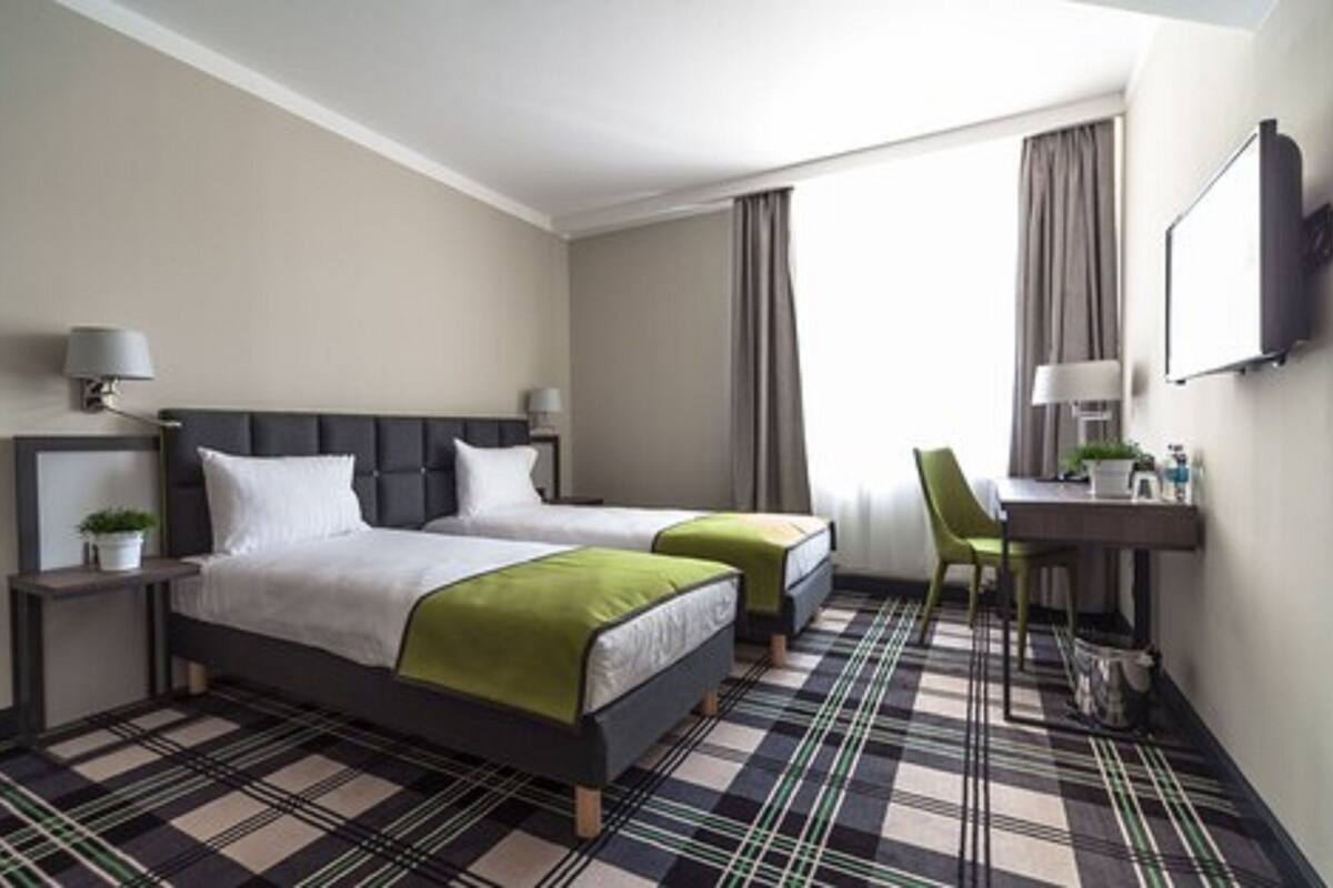 A hotel room with two beds, a desk, a chair, a TV, and a check-in counter.