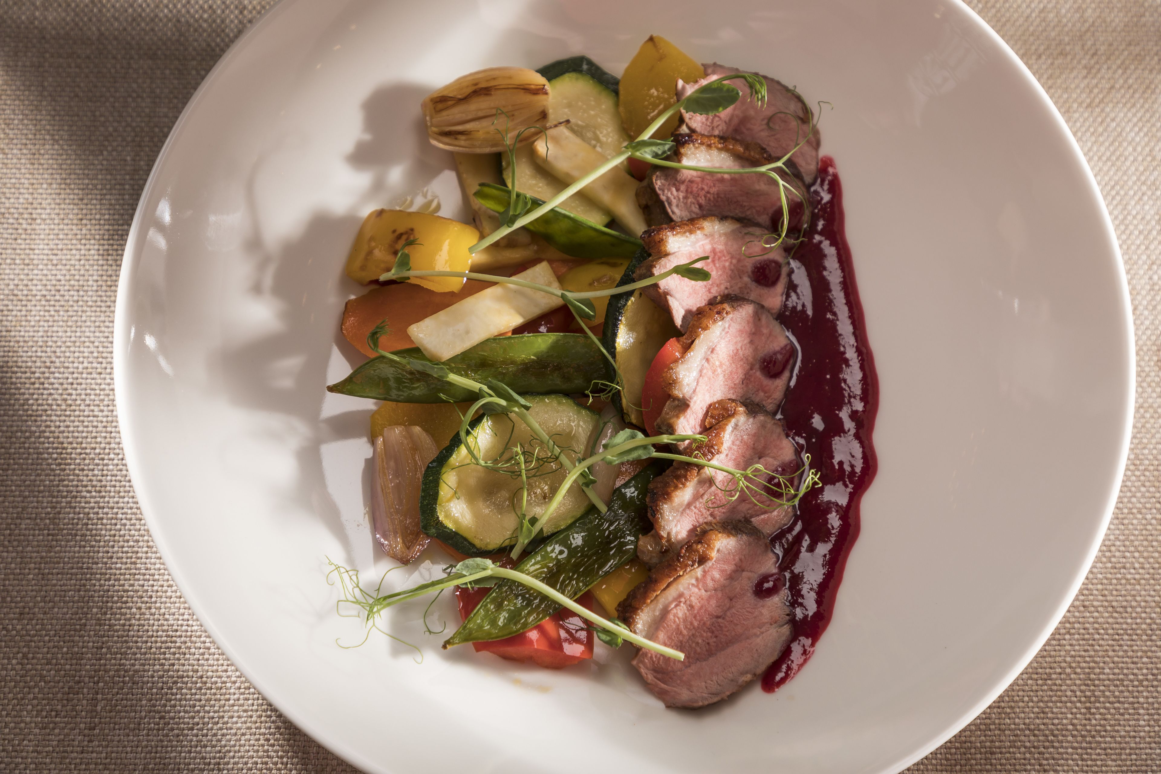 Ein weißer Teller mit geschnittenem Fleisch, Gemüse und roter Soße.