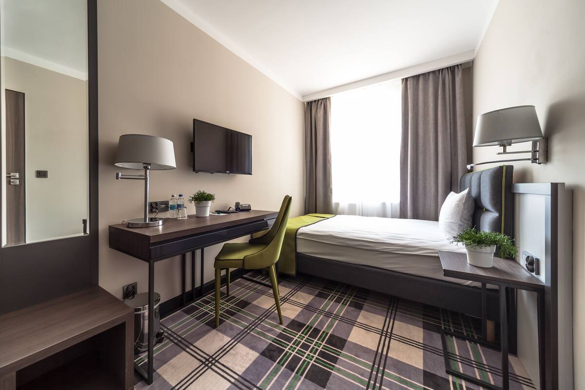 A hotel room with a bed, desk, chair, TV, and a window with curtains.