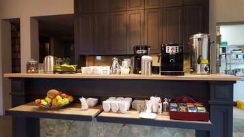 Una encimera de cocina con cafeteras, una jarra de leche y un frutero.