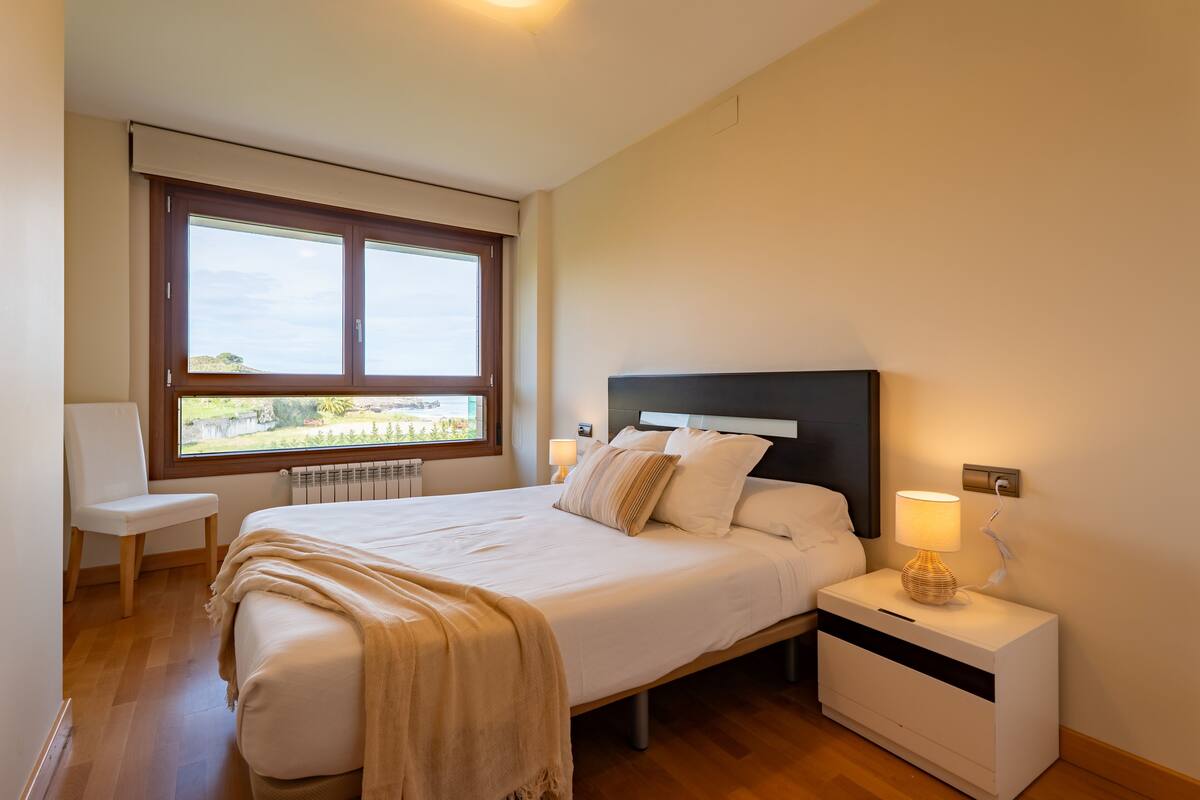 A bedroom with a large bed, bedside tables, a chair, and a window with a view.