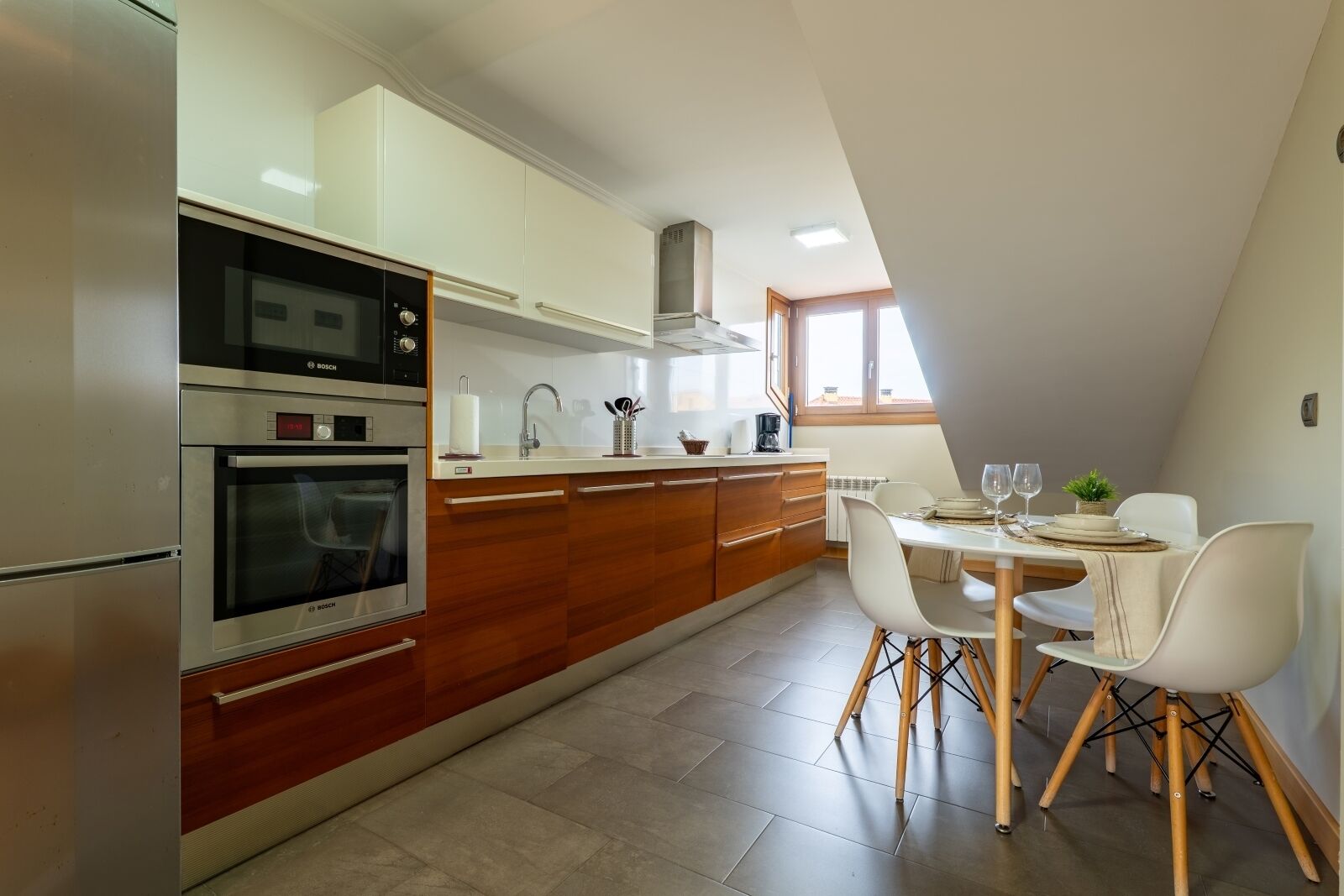 A modern kitchen with a dining area, featuring a Bosch oven, white cabinets, and a dining table with chairs.
