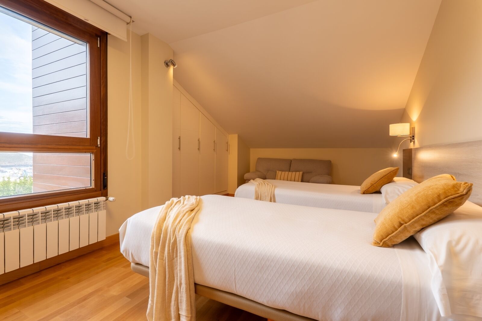 Un dormitorio con dos camas, una ventana con persianas, un radiador y un cabecero con lámpara.