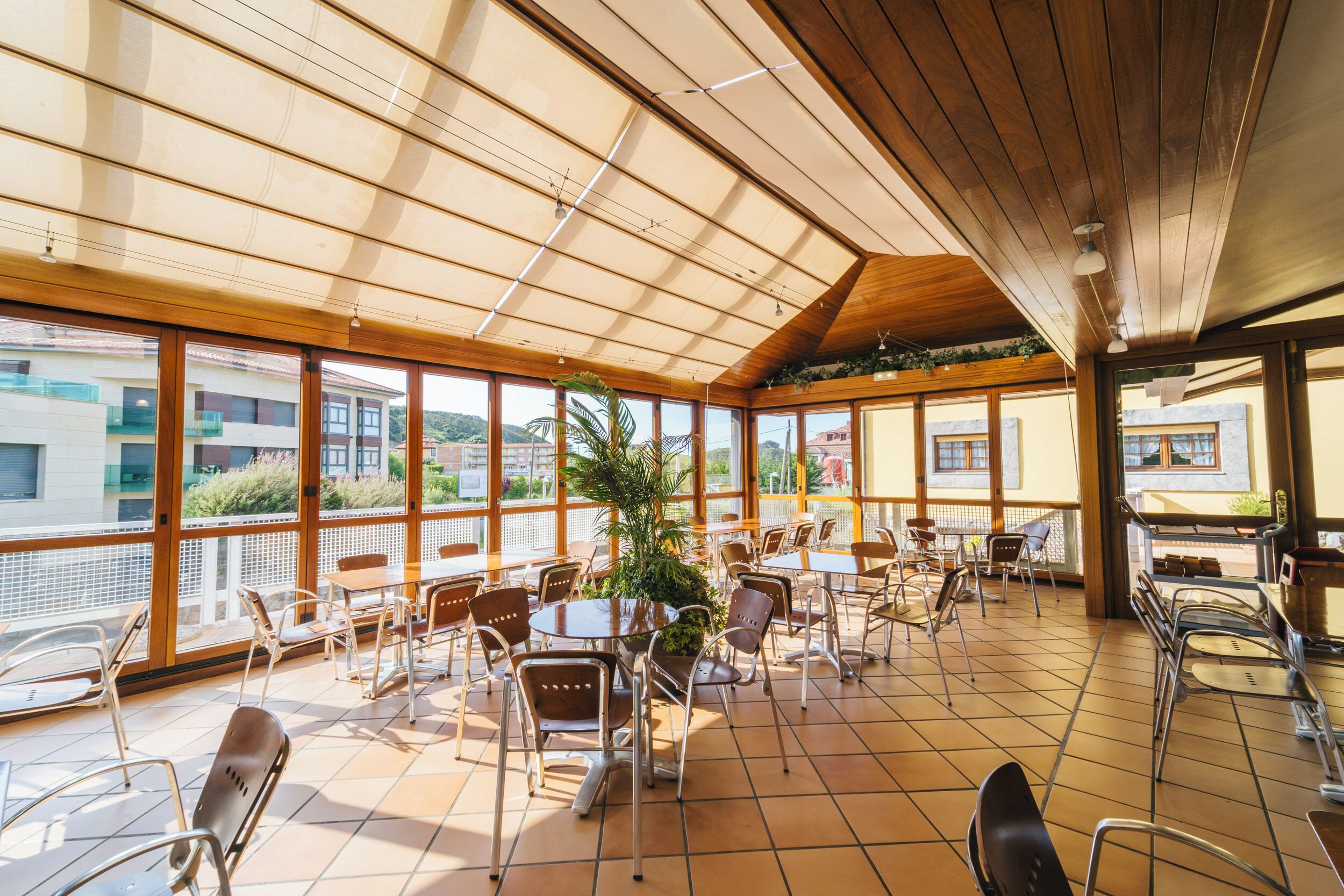 Un espacio interior amplio con ventanas grandes, techo de madera y varias mesas y sillas.