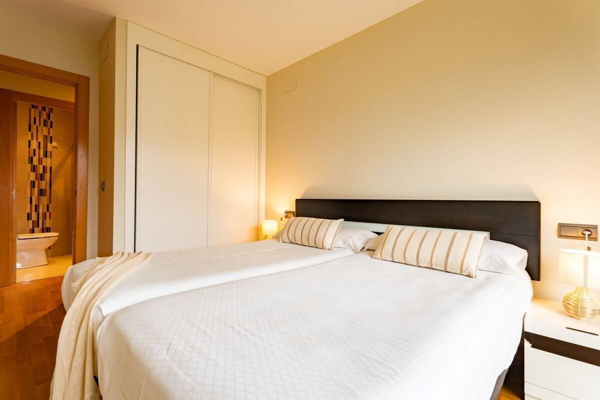 A neatly made bed with a dark headboard, a bedside lamp, and a small bedside table with a lamp.