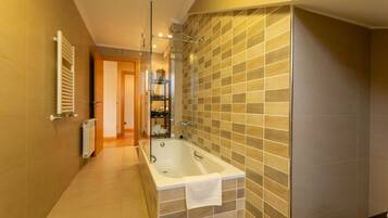 A modern bathroom with a freestanding bathtub, a glass shower enclosure, and a tiled wall.