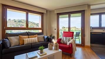 Ein modernes Wohnzimmer mit einer schwarzen Ledersofa, einem roten Sessel und einem weißen Couchtisch. Große Fenster bieten Blick auf eine grüne Landschaft.
