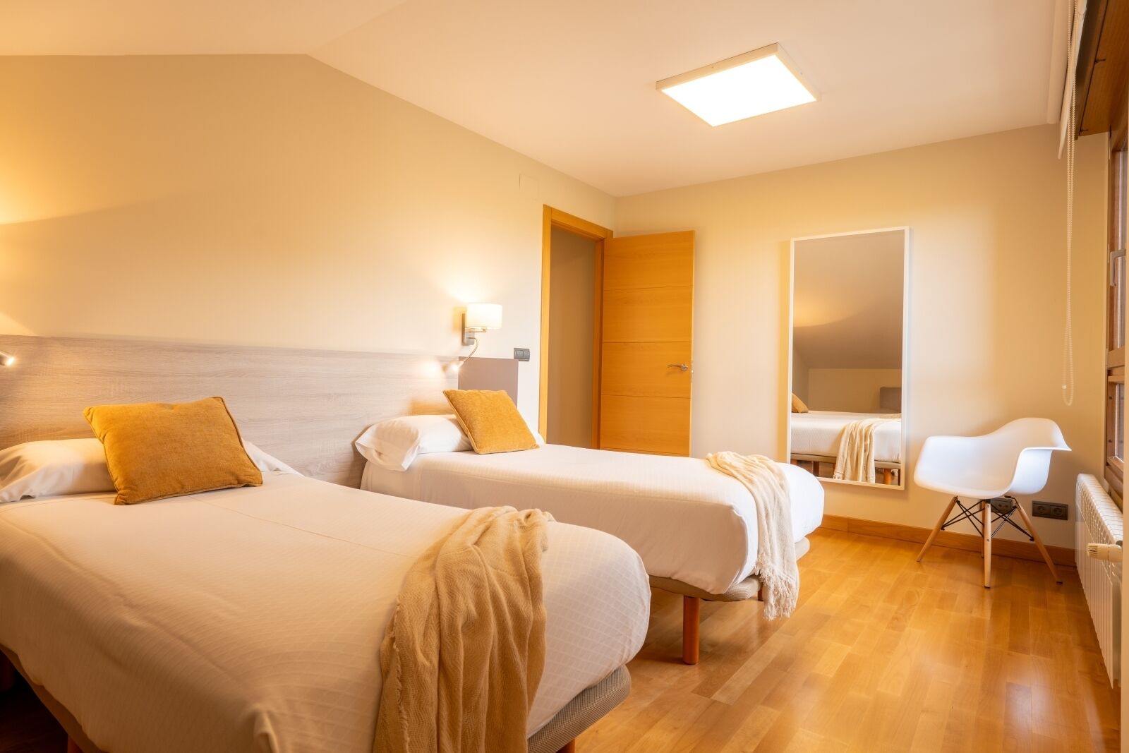 Una camera d'albergo con due letti, un'armadietto in legno, una sedia bianca e un grande specchio.
