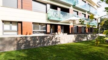 A modern multi-story residential building with balconies, large windows, and a well-maintained lawn.