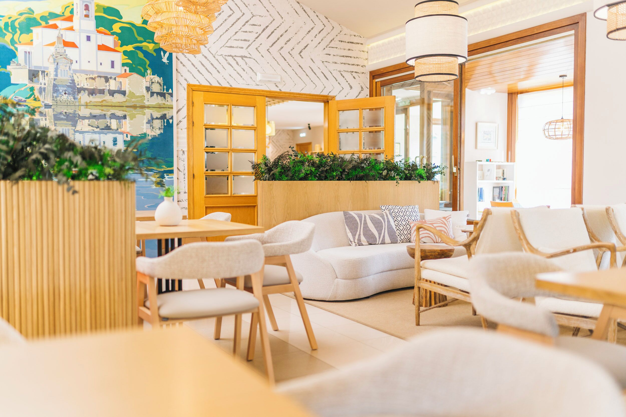 A modern hotel lobby with a reception desk, seating area, and a mural of a coastal town.