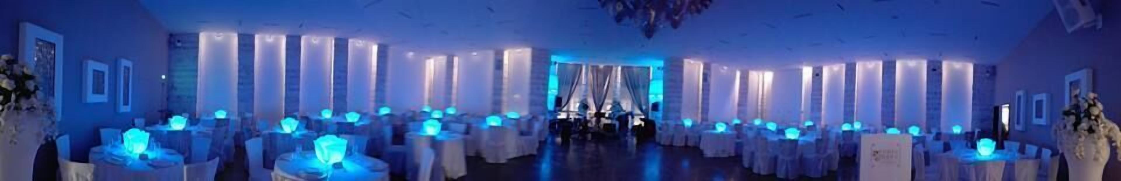 Una habitación con varias mesas redondas cubiertas con manteles blancos e iluminación azul.