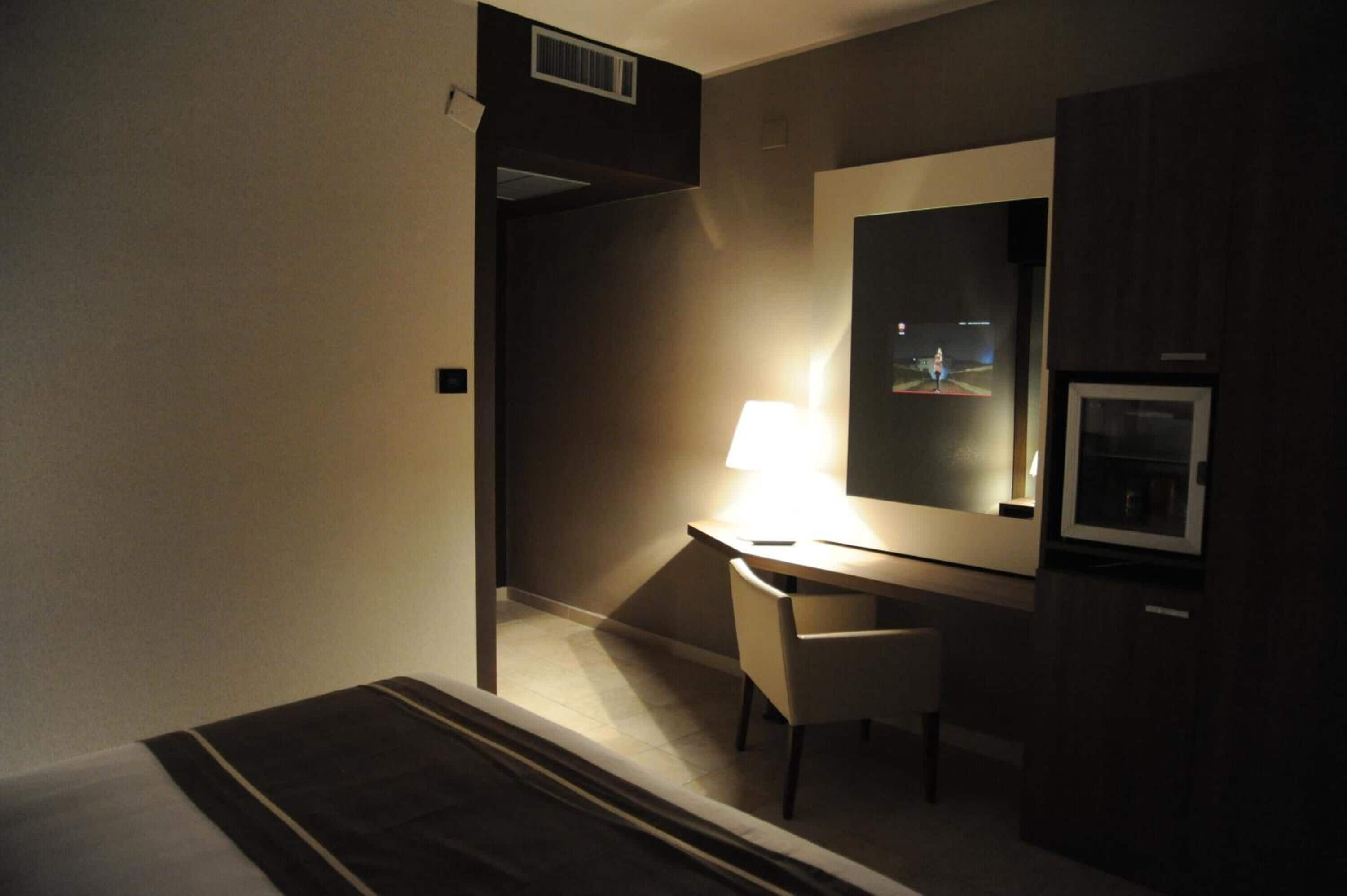 A hotel room with a desk, chair, and a large mirror.