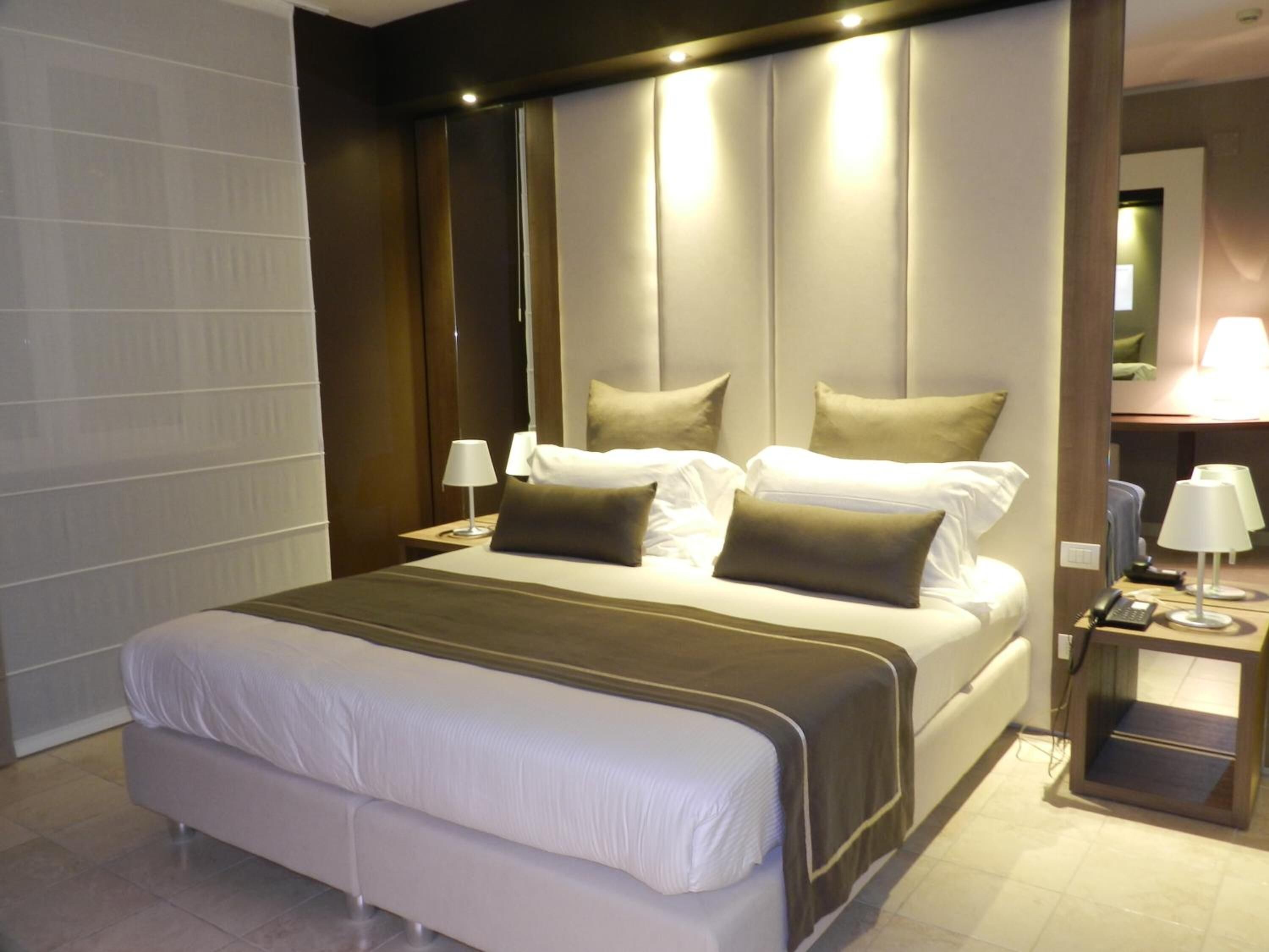 A modern hotel room with a large bed, bedside tables, and a mirror.
