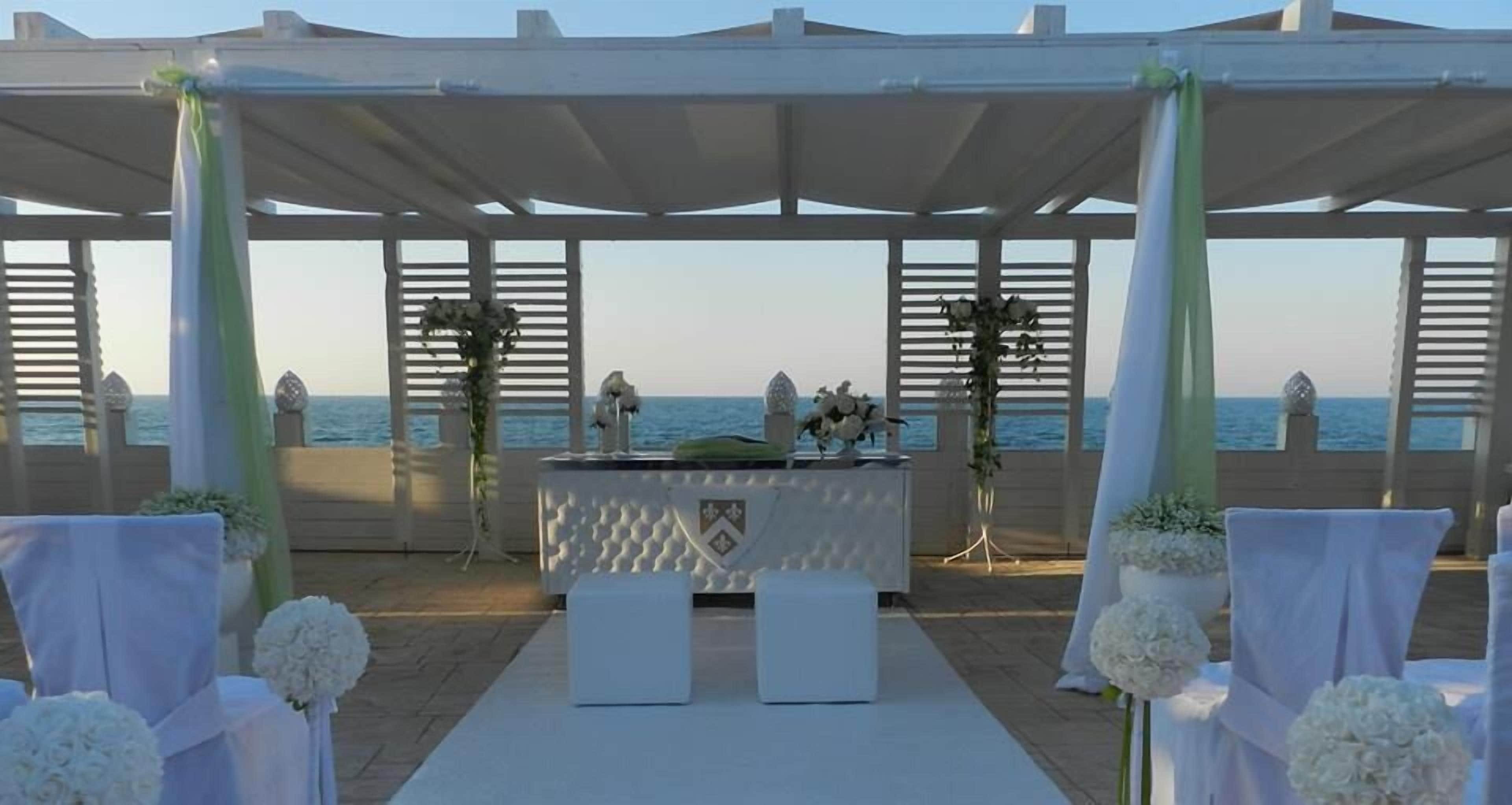 An outdoor wedding setup with a white altar, white chairs, and a view of the sea.