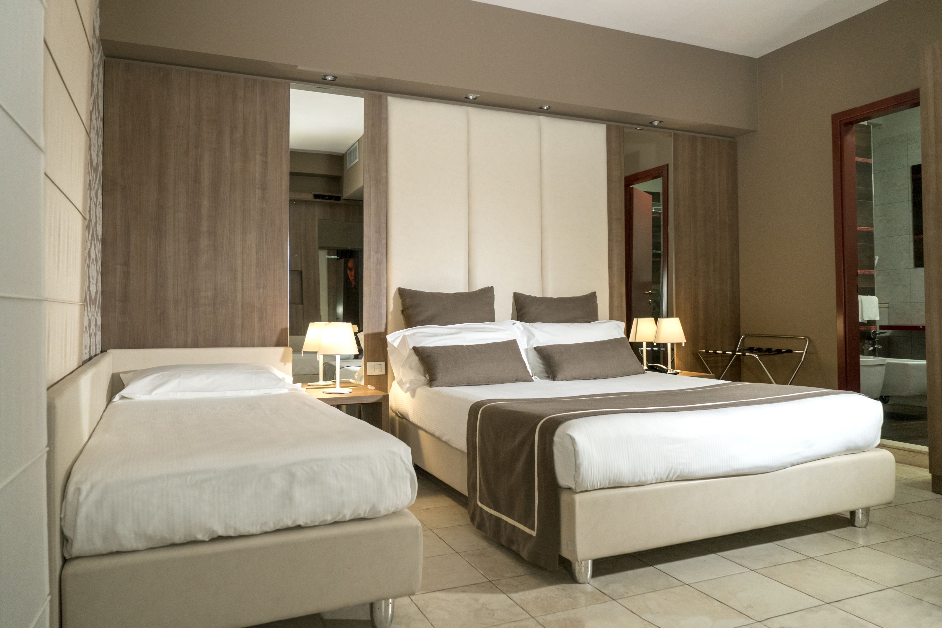 Une chambre d’hôtel avec deux lits, un grand miroir et une salle de bain visible à travers une porte ouverte.