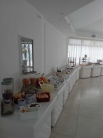 Montaje de bufé con diversos alimentos y bebidas, una vitrina de vidrio y un área de estar con sillas.