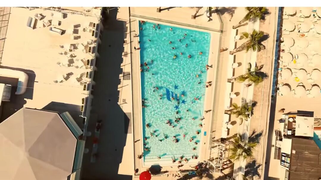 An aerial view of a swimming pool surrounded by sun loungers and palm trees.